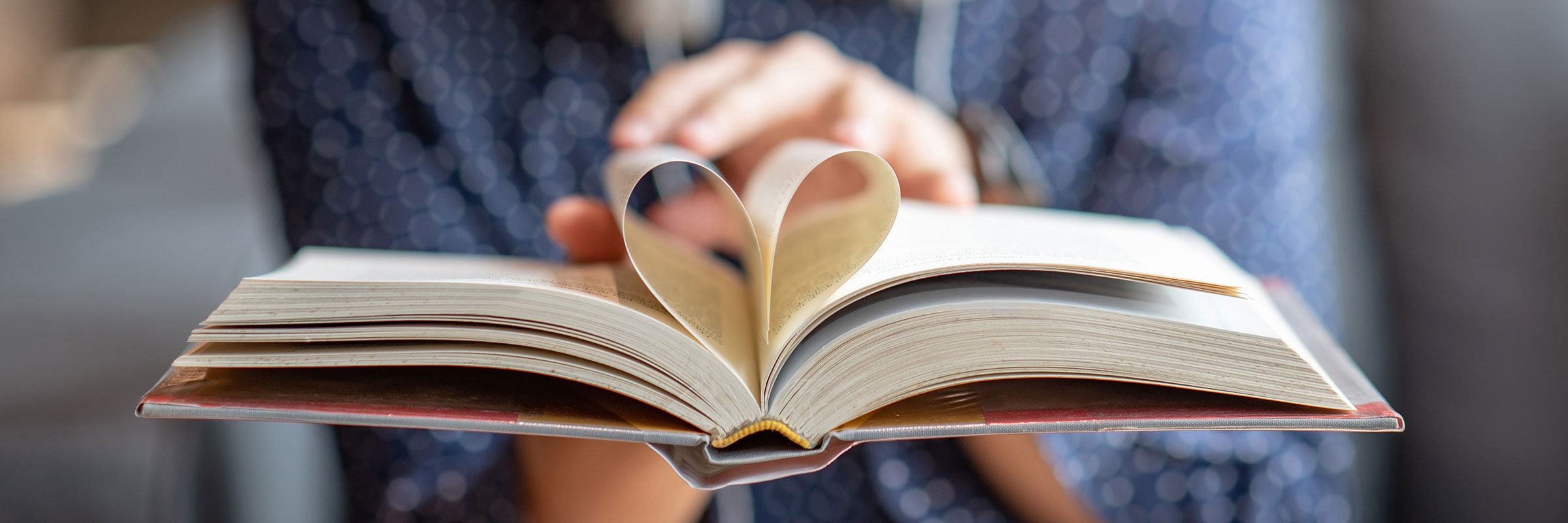 Hands holding book with middle pages curled into heart shape